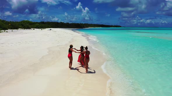 Pretty fun women on photoshoot enjoying life on the beach on clean white sand and blue 4K background alt
