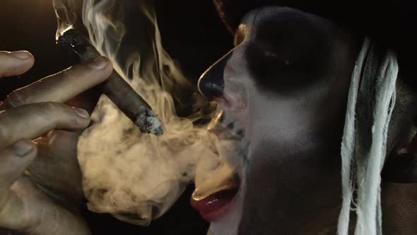Scary Guy in Carnival Costume of Halloween Skeleton Smoking Cigar, Making Faces, Showing Tongue alt