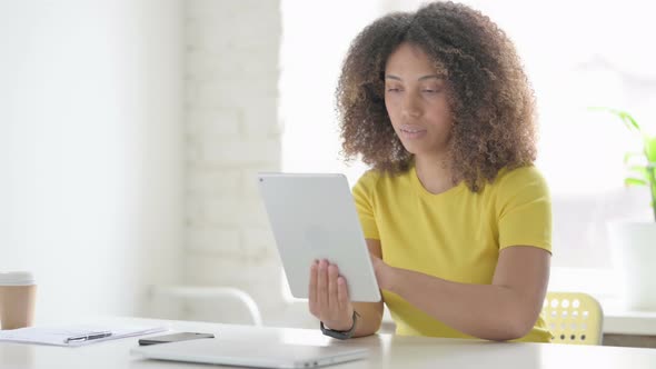 African Woman Celebrating Success on Tablet in Office alt