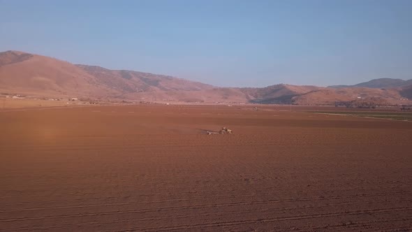 Aerial, Tractor in distance plowing field with California mountain background alt