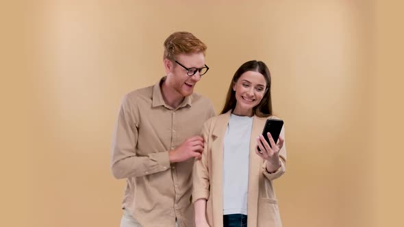 Man and Woman Holding Smartphone and Smiling at Each Other Positive Online Communication Over Beige alt
