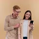Man and Woman Holding Smartphone and Smiling at Each Other Positive Online Communication Over Beige - VideoHive Item for Sale