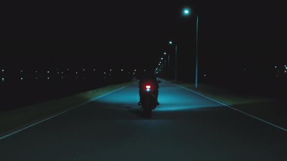 A Man Moving Away on a Sports Motorcycle Into the Distance Against the Backdrop of a Night City alt