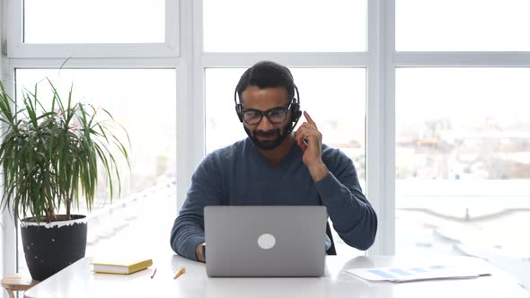 Indian Male Employee Wearing Headset and Eyeglasses Making Online Consultation
