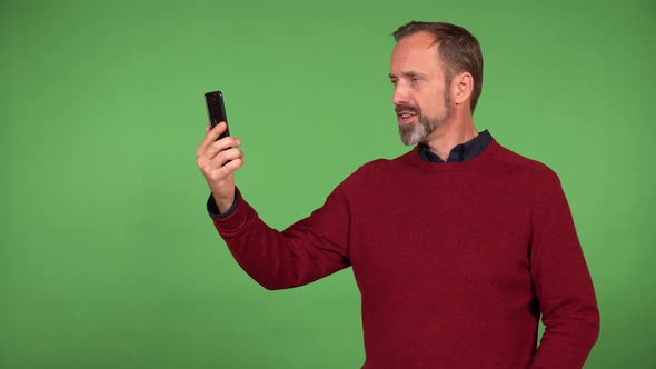 A Middleaged Caucasian Man Talks on a Video Call on a Smartphone with a Smile  Green Screen