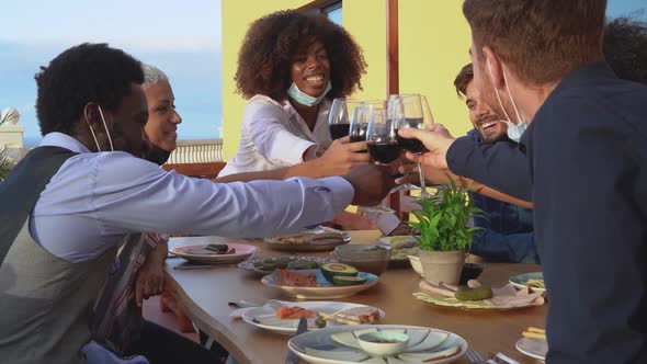 Young friends toasting with red wine glasses at dinner appetizer during sunset time alt