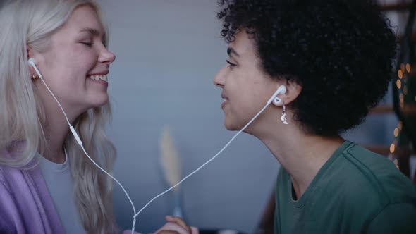 Young Girls Listen Music in Same Headphones and Hold Hands Dancing and Smiling
