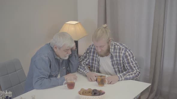 Positive Caucasian Adult Son and Mature Father Listening To Music Together. Smiling Men Putting on alt