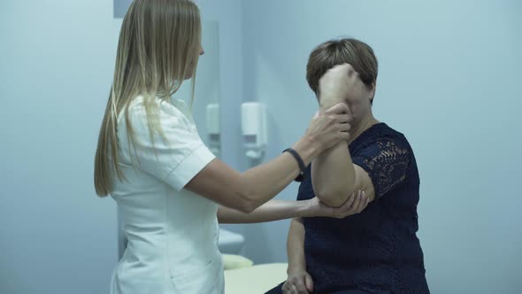 Professional Caucasian Doctor Checking Arm of an Elderly Woman Sitting in the Office alt