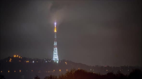 Beautiful night time lapse: illuminated television tower covered by stormy clouds.