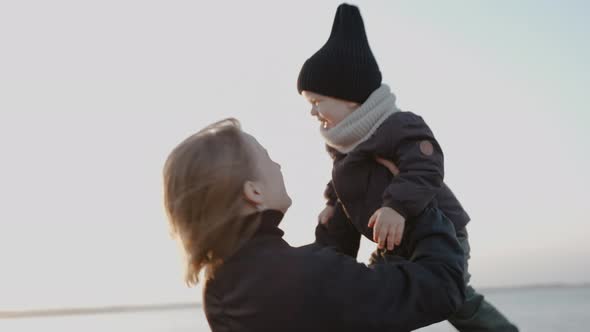 Happy Woman Raises Her Child to the Sky on the Shore of Lake on a Fall Evening alt