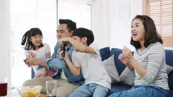 Happy Asian family funny playing video game with technology console on sofa in living room at house. alt