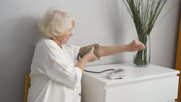 Senior Caucasian Woman Checking Blood Pressure with Electric Monitor Tonometer at Home