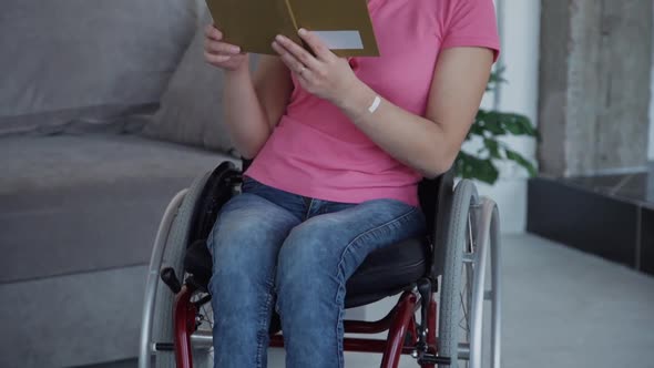 Young Handicapped Woman Reading Book Sitting in Wheelchair at Home Room