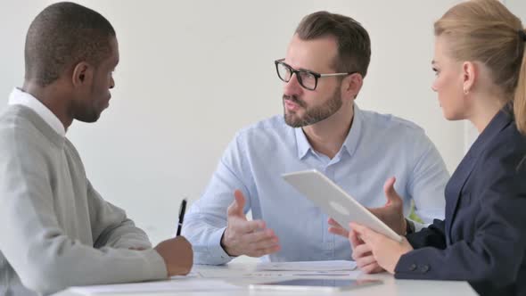 Businessman Talking to Colleagues Using Tablet and Taking Notes alt