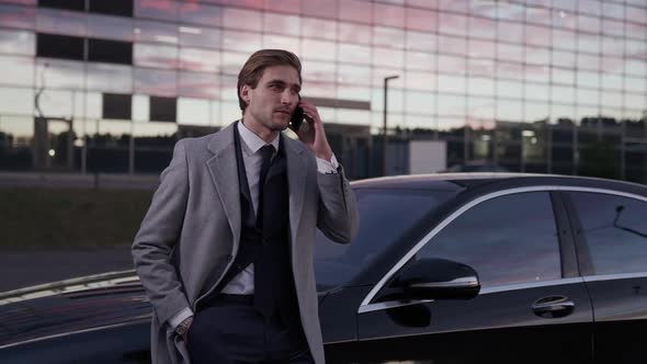 Young Businessman Standing Near a Business Car and Talking on a Mobile Phone Top Manager in a Suit alt