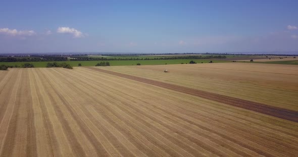 Drone Flying Over Large Fields With A Working Combine In The Summer