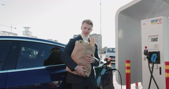 Handsome Businessman Relies on a Blue Luxury Electric Car That Is Charging alt