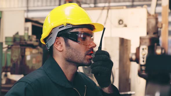 Factory Worker Talking on Portable Radio While Inspecting Machinery Parts alt