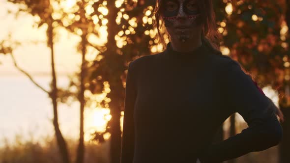 A Young Woman with Santa Muerte Makeup Dressed in a Black Dress of Death Walks Against the Backdrop alt