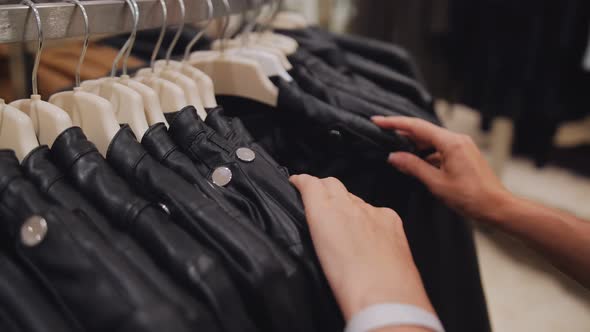 Closeup of Women's Hands in a Clothing Store Choosing a Leather Jacket on Hangers