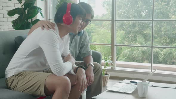 Happy father and son wearing headphone sitting on sofa video call with family on laptop computer. alt