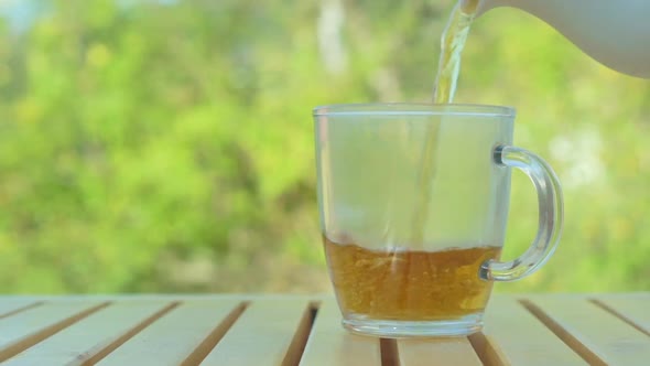 Tea pouring into cup from teapot on green nature background