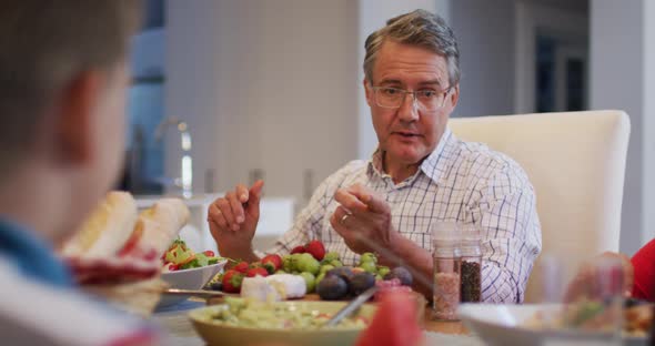 Smiling caucasian grandfather talking to grandson at table during family meal alt