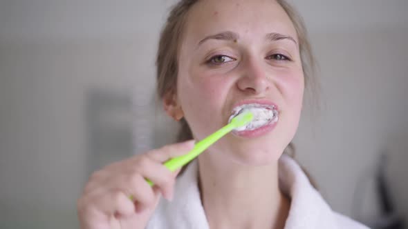 Closeup of Brunette Young Woman with Brown Eyes Brushing Teeth in Slow Motion Smiling Looking at alt