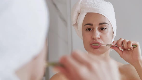 Attractive Woman with Towel on Head Brushing Teeth in Front of the Mirror alt