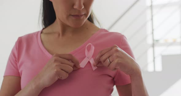 Happy asian woman in pink tshirt showing pink ribbon at home alt