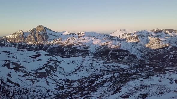 Aerial View Zooming Out of Vast Snowy Mountainous Landscape During Golden Hour alt