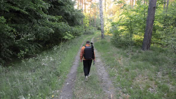 Aerial Drone View Following Young Caucasian Man with Backpack Walking through Forest