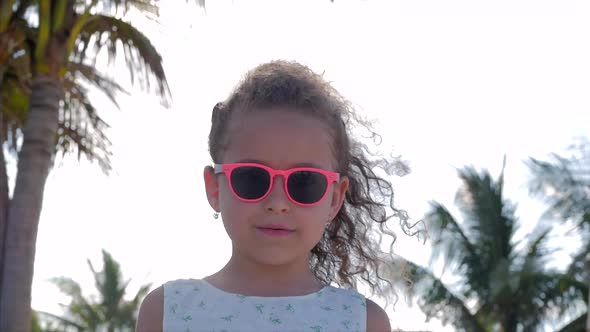 Close-up Portrait of a Beautiful Little Girl in Pink Glasses, Cute Smiling, Looking at the Camera alt