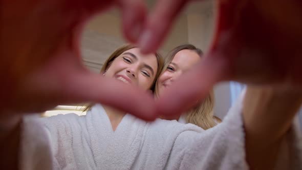 Two Happy Smiling Beautiful Blonde Women Showing Hands Sign Heart Shape Looking at Camera Healthy