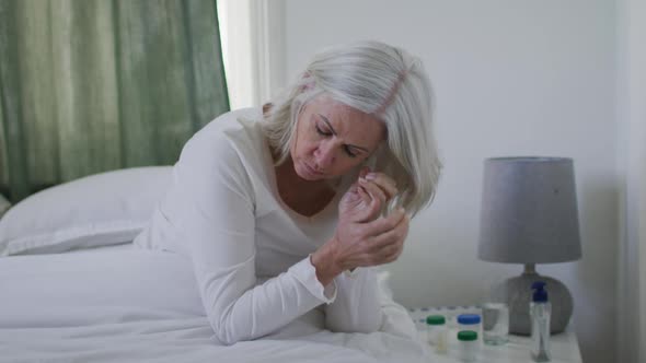 Sick or depressed senior caucasian woman sitting up in bed at home and holding her head alt