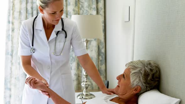 Female doctor checking senior woman pulse during check up in bedroom alt