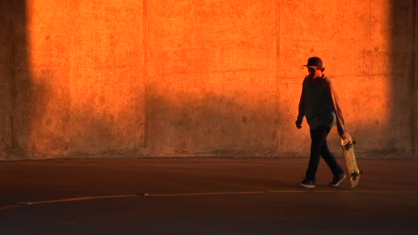 Silhouette of a young man skateboarding in a parking garage at sunset. alt