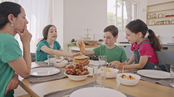 Mother and three kids eating breakfast of pancakes and fruits alt
