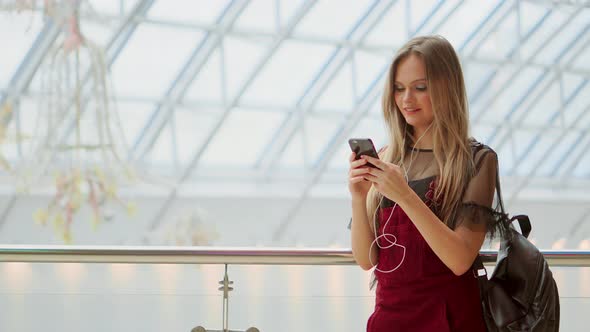 Happy Teenage Girl Holding Bags with Purchases, Smiling While Looking at Phone in Shopping Center alt