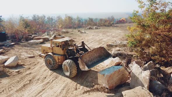 professional yellow bulldozer with a bucket is working in the quarry with stones alt
