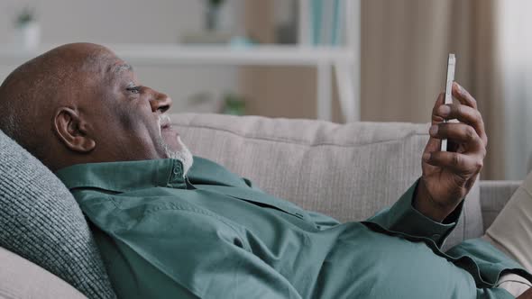 Close Up Relaxed Lying on Couch Elderly African American Man Making Video Call Use Smartphone Mature alt