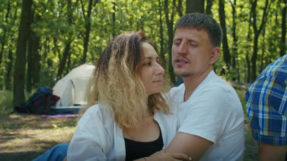 Two Young Couples Man and Woman Enjoy Their Vacation in the Forest While Playing the Guitar the