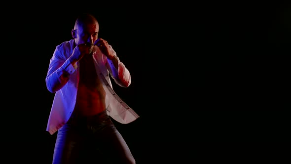 a Man in Jeans and an Unbuttoned White Shirt is Boxing on a Dark Background alt