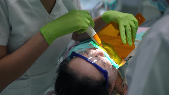 High Angle View of Caucasian Woman in Dental Chair with Unrecognizable Doctor and Nurse Using UV alt