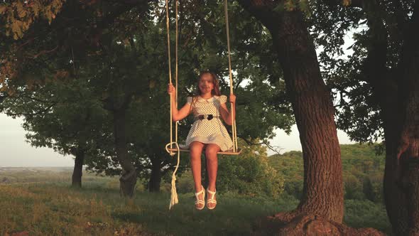 Beautiful Young Girl Swinging on a Swing Under a Tree in the Sun alt