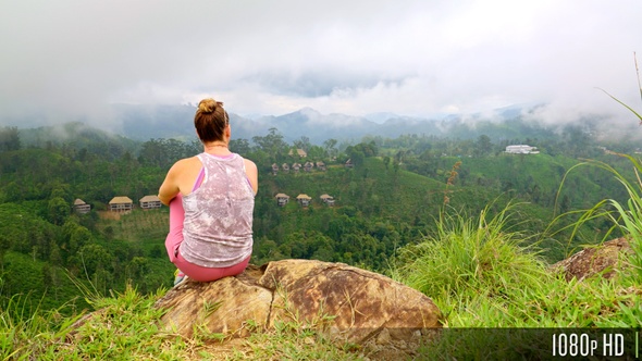 Woman admiring the view from the edge of a rock cliff in the cloudy highland mountains alt