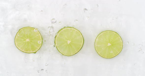 Drops of Water Fall on Three Pieces of Lime Lying on a White Background alt