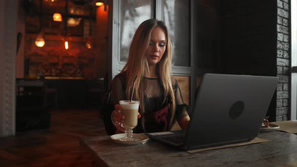 Side View. Young Business Woman Sitting at Table and Taking Notes in notebook.On Table Is Laptop alt