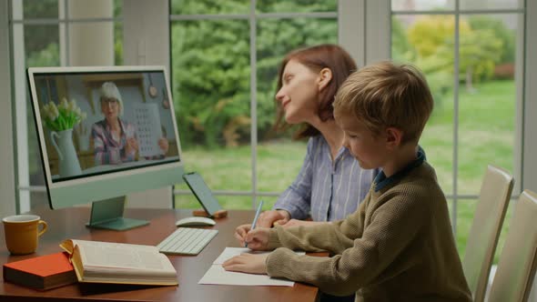 Young 30s Mother Helping Her Son with Online Lesson at Home alt